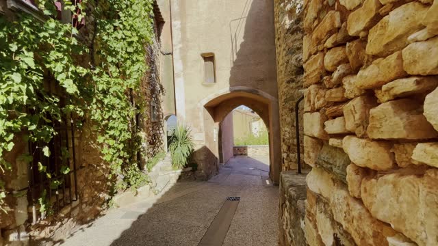 Small romantic old alley in a small village in France with old stone walls and lots of plants and archway in good weather