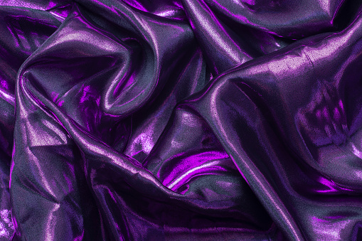 Abstract wrinkled purple dark fabric. Shiny luxury cloth texture for the background.