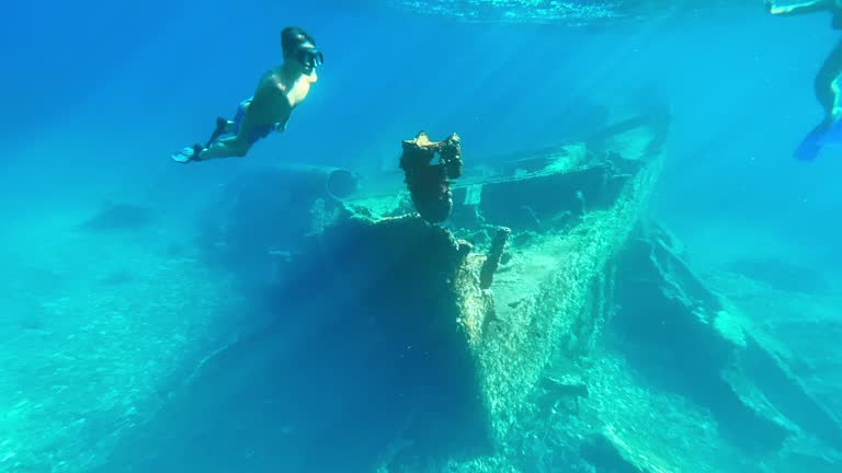 Boy swimming along a sunken ship on the sea bottom in sunshine