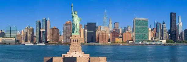 Photo of Statue of Liberty and New York City Skyline with UN Building, Chrysler Building, Empire State Building and Skyscrapers of Manhattan East Side in the Morning, NY, USA.