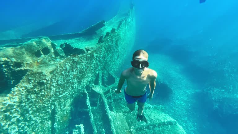 Boy wearing a mask and diving to the ship on the bottom of the sea