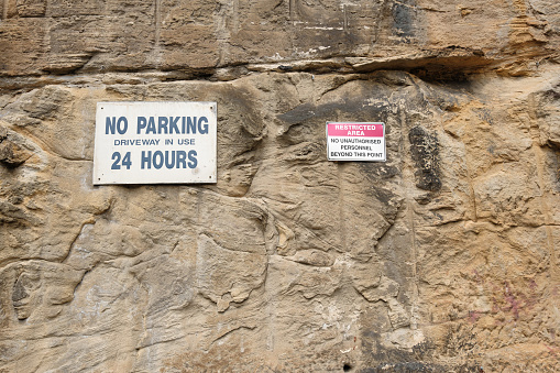 Old No parking and restricted area signs on a rough, stained rock wall.