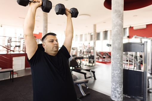 A middle aged man is training with dumbbells in a gym, he is determined to lose weight