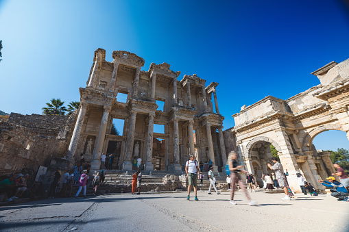 Visitors exploring the ruins of the Library of Celsus, a historic Roman building in Ephesus, Turkey, on a sunny day.