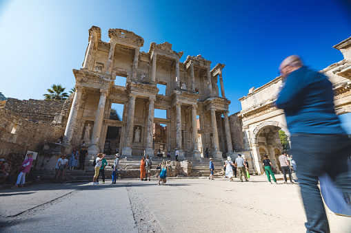 Travelers visiting the historical Library of Celsus ruins in Ephesus, Turkey on a bright sunny day.