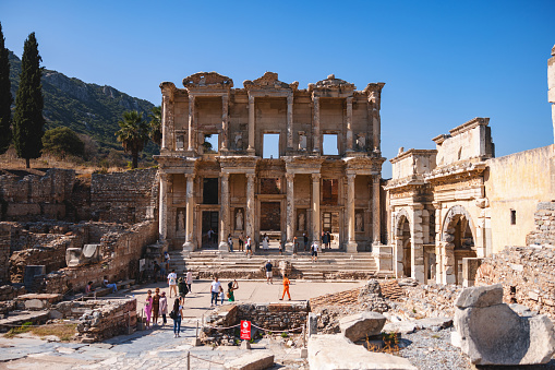 Tourists explore the ruins of the Library of Celsus in Ephesus, Turkey, under a clear blue sky on a sunny day.