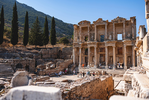 Tourists explore the ruins of the famous Library of Celsus in the historic city of Ephesus, Turkey, under a clear blue sky.