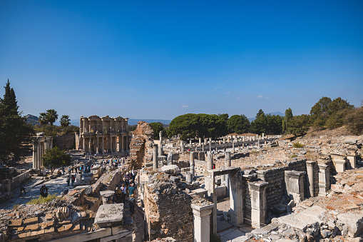 Wide shot of visitors exploring the ruins of the Ancient Greek Theatre in Ephesus, Turkey under clear blue skies.