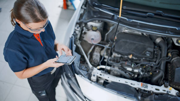 Female Mechanic Using Mobile Phone Next To Car Engine At Auto Repair Shop Female Mechanic Using Mobile Phone While Standing Next To Car Engine At Auto Repair Shop car mechanic top view stock pictures, royalty-free photos & images
