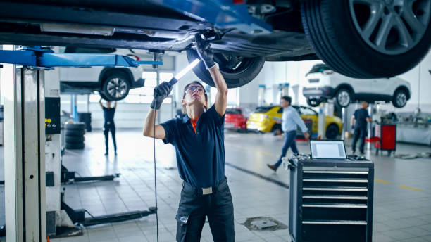 Female Mechanic With Light Working Under Car In Auto Repair Shop Female Mechanic Uses A Light Source While Working Underneath A Car In The Auto Repair Shop mechanic working under car stock pictures, royalty-free photos & images