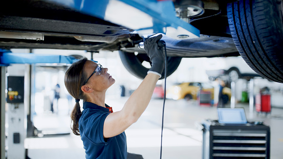 Female Mechanic Working Underneath Car On Hydraulic Platform In Auto Repair Shop