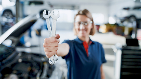 Female Mechanic Confidently Holds Wrenches Next To A Car Engine In The Auto Repair Shop