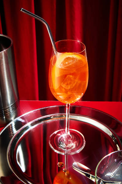 foto ravvicinata di bicchiere alto pieno di cocktail all'arancia, aperol con cubetti di ghiaccio con pezzo di agrumi e paglia seduto su vassoio d'argento. - martini brand vermouth foto e immagini stock