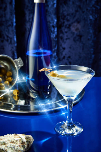 bicchiere riempito di martini, guarnito con due olive verdi, vassoio d'argento con olive e bottiglia su sfondo blu. concetto di capodanno. - martini brand vermouth foto e immagini stock