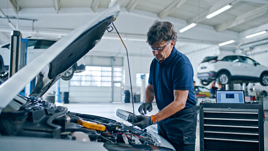 Male Mechanic Operating A Diagnostic Device Connected To Car Engine In Auto Repair Shop,Ensuring A Thorough Inspection For Optimal Performance