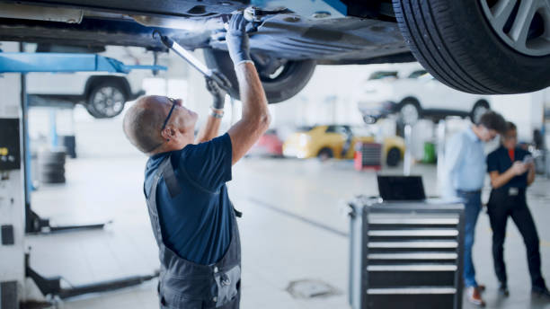 Male Mechanic With Light Working Under Car In Auto Repair Shop Male Mechanic Uses A Light Source While Working Underneath A Car In The Auto Repair Shop mechanic working under car stock pictures, royalty-free photos & images