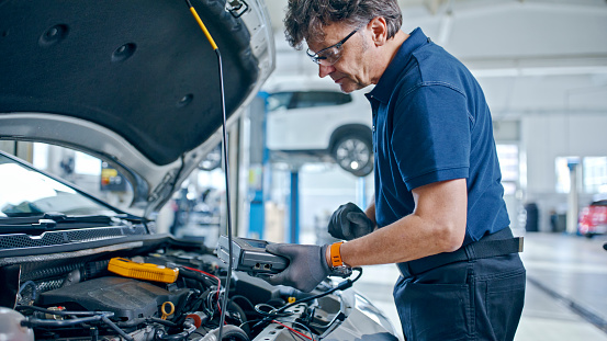 Male Mechanic Operating A Diagnostic Device Connected To Car Engine In Auto Repair Shop,Ensuring A Thorough Inspection For Optimal Performance