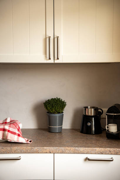 istock Partial view of a kitchen with white wall and base cabinets (country house style) and brown worktop.  Kitchen herbs, milk frother, espresso machine and a bowl covered with red checkered cloth 1892191965