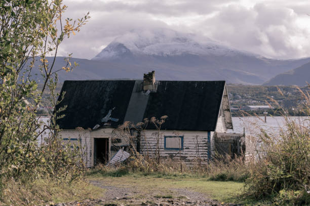 A hauntingly beautiful scene of snow-covered mountain peaks, seen through the window of a ruined cabin in a ghost village. The clear blue sky and bright sunlight enhance the serene yet eerie atmosphere of this abandoned place, capturing the essence of nature's quiet majesty and the passage of time.