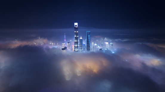 High angle view of Shanghai Lujiazui landmarks in foggy night, colorful modern buildings above clouds, drone view.