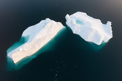 Melting icebergs by the coast of Greenland, on a beautiful summer day - Melting of a iceberg and pouring water into the sea. Global warming\nArctic nature landscape, Summer day