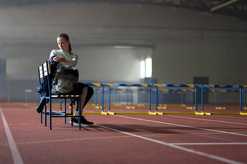 Thoughtful young woman sitting on bench during sports training in sports hall.