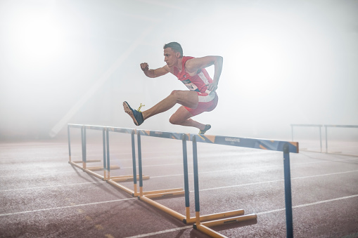 Athlete man jumping over hurdles during practice in sports hall.