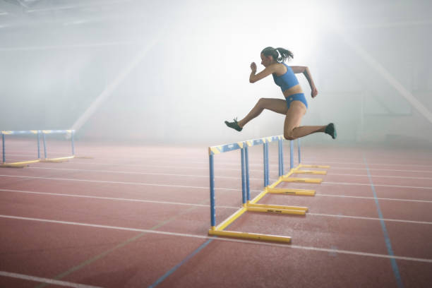 Fast, hurdles and team of women on track running in race, marathon or competition in stadium. Fitness, workout and female athletes jumping with speed and energy for outdoor training with blur motion.