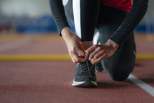 Female athlete tying shoelaces on her running shoes in sports hall.