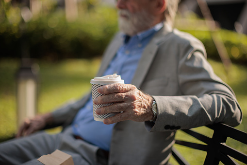 Close-up of a senior businessman's hand holding a paper coffee cup during a break in the park.