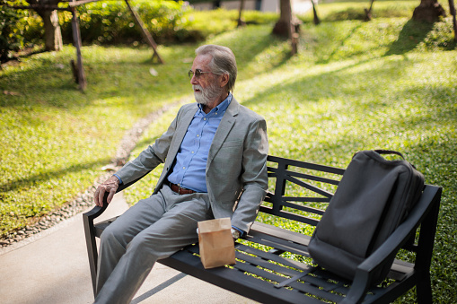 Senior businessman is sitting tired on a park bench during his work break.