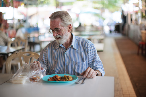 Senior man enjoying local Thai food at the food court in Bangkok.