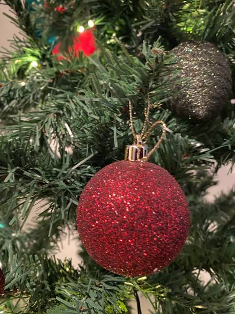 istock Glittery Red Bauble Christmas Decoration in Foreground on Artificial Tree Lights and other Bauble Decorations in Background Happy Holidays 1892326337