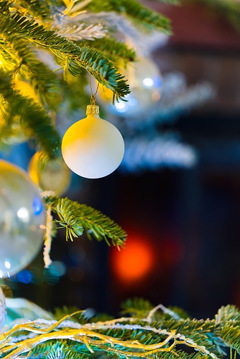 Immerse in the holiday spirit with this enchanting photo featuring baubles on a Caucasian Fir. Blurred Christmas lights and festive decor enhance the cozy atmosphere, while a red brick fireplace adds warmth and charm to the scene.