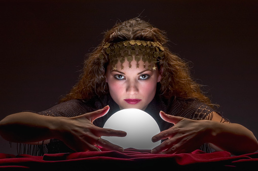 Fortune teller with Cristal ball on red velvet. Looking at camera.