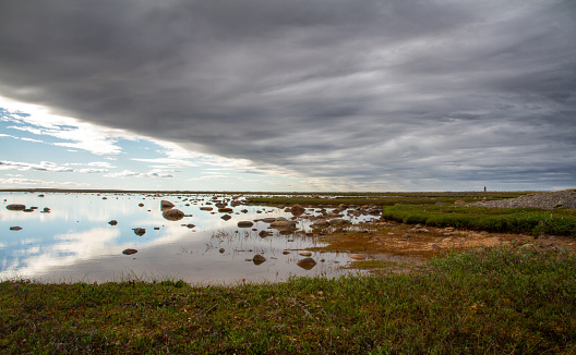 Flat arctic landscape in the summer with partly overcast skies and a pond in the foreground, near Arviat Nunavut Canada