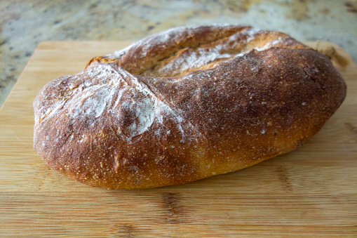 Slicing fresh homemade bread made of sourdough. Homemade baking concept. Artisan bread with golden crispy crust.