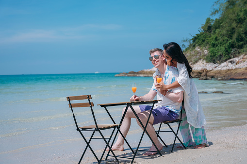 Happy and loving young couple drink orange juice at tropical beach. Couple Enjoying Fun and Romance by the Ocean