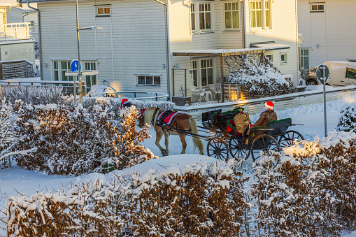 Sweden. Uppsala. 12.24.2023. Winter scene with horse drawn by sleigh, on which Santa Claus rides with bag of gifts, along road among villas.