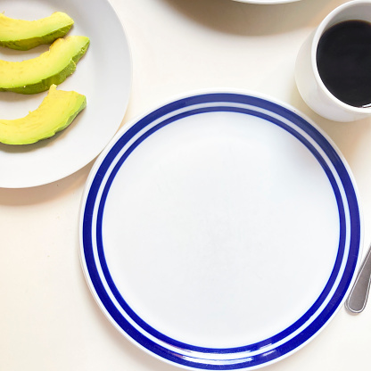 High angle view of empty plate on table with slice of avocado and cup with black coffee