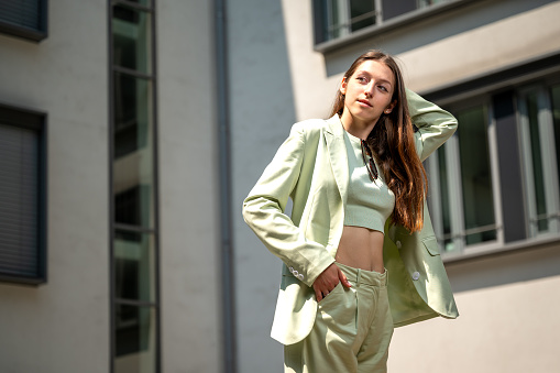 Beautiful young woman poses in an elegant green suit having business buildings in the background