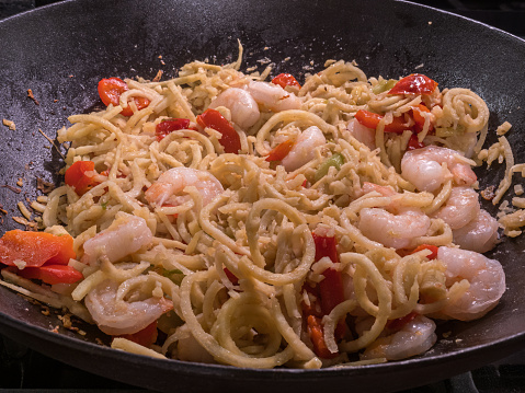 Spiralized butternut squash twirls dancing with sizzling shrimp and vibrant red peppers in a seasoned cast iron pan.