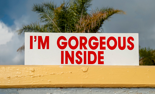 Sign stating I'm Gorgeous Inside in red letters used on a real estate sales sign. Image can be used for other purposes