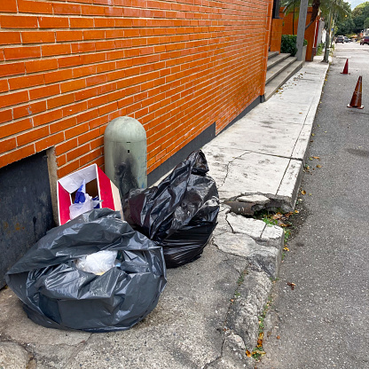 Black plastic bag with garbage over a sidewalk in a suburb of Caracas city
