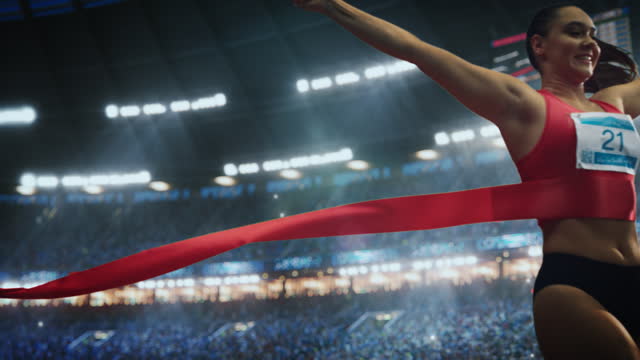 Cinematic Slow Motion Footage of a Runner with Speed Ramp Effect. Strong Female Athlete is Sprinting Towards the Line in a Crowded Stadium, Crossing the Race Finish with Her Hands in the Air