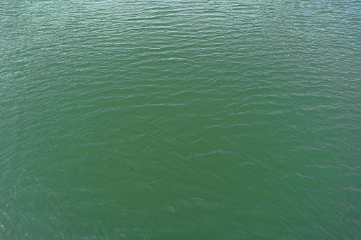 River from above, ocean water surface aerial view, water texture background, light blue green reflection on lake wave ripples flat surface. Sun light reflecting or sparkling glitter on water.