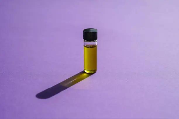 Small bottle of essential oil standing upright on a bright purple background with light shining through it