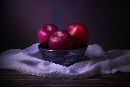 Red apples in a ceramic bowl sits on top of a table. Still life with fruits