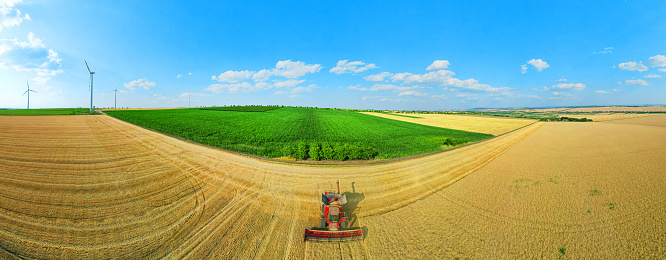 combine in the field of wheat and 360 summer panorama with blue sky. and with wind turbines in the background.