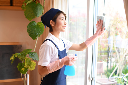 Young Asian female housekeeper cleaning windows